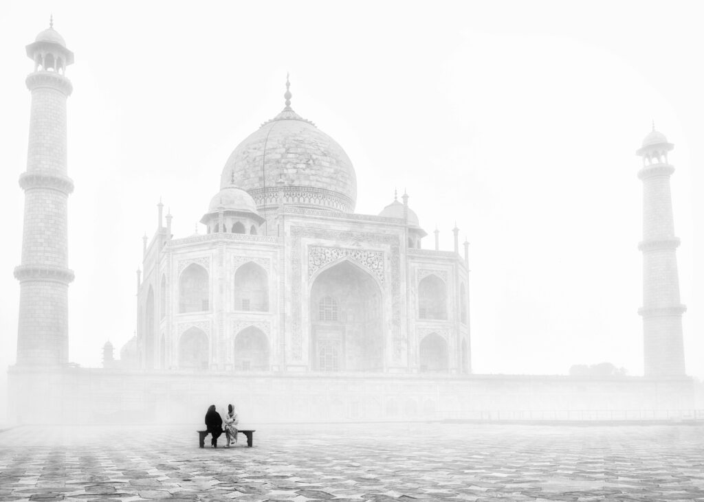 Two people sit before the foggy Taj Mahal, capturing its serene beauty.
